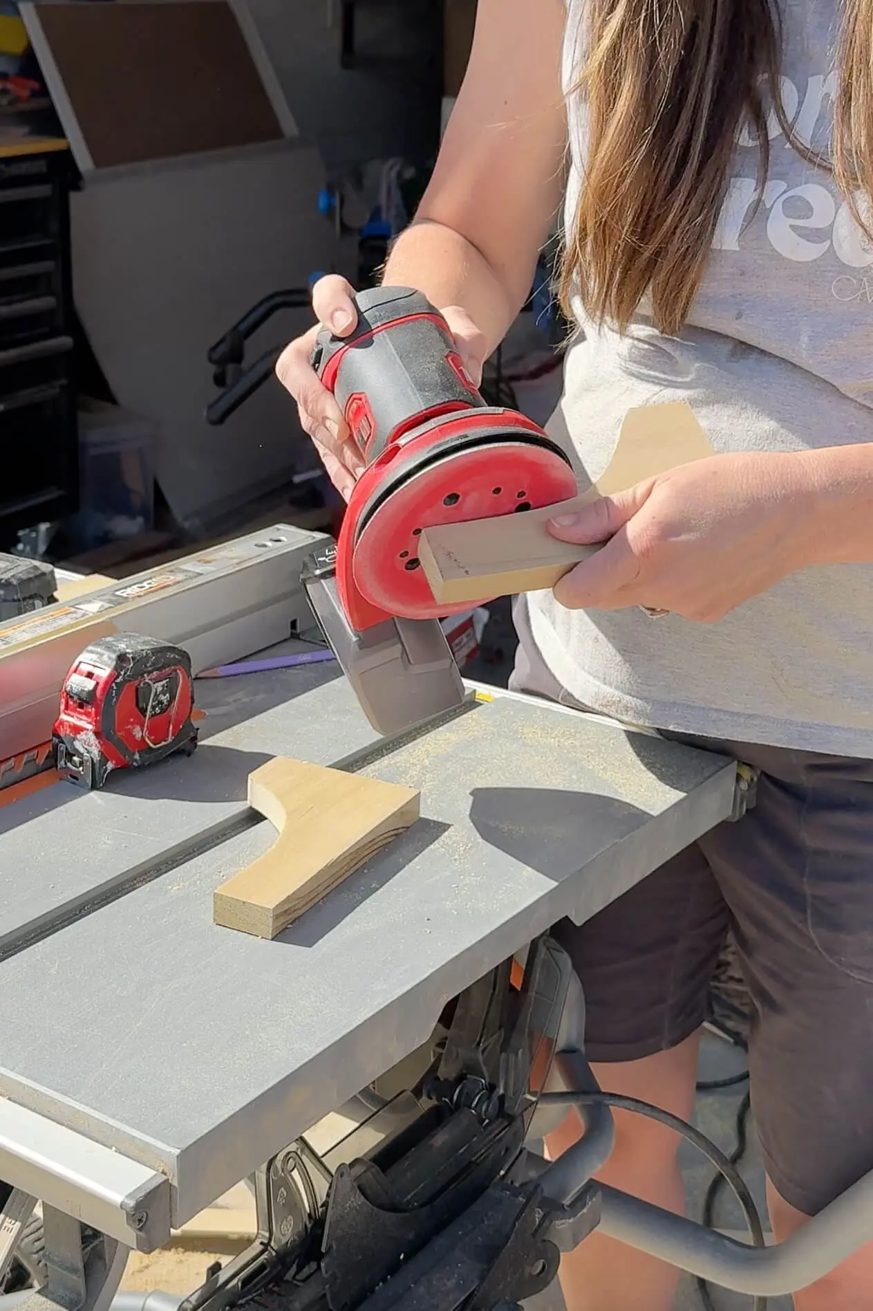 Sanding a curved wood bracket for a built-in headboard with storage using a red orbital sander.